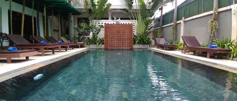 Una piscina al aire libre, sombrillas, sillones reclinables de piscina