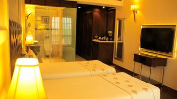 A hotel room with a bed, a TV, a lamp, and a bathroom visible through a glass door.