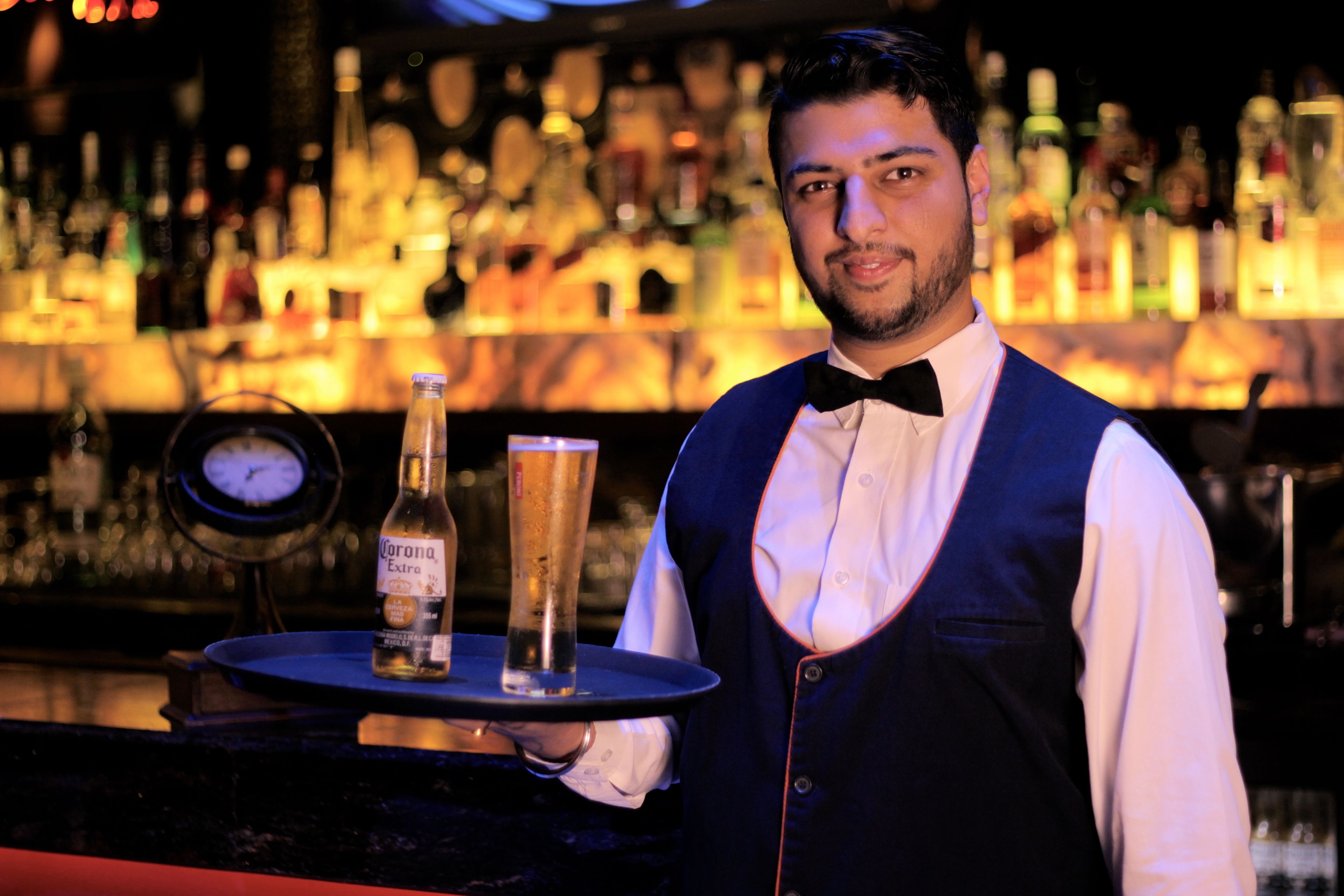 Ein Barkeeper hält ein Tablett mit einer Flasche und einem Glas.