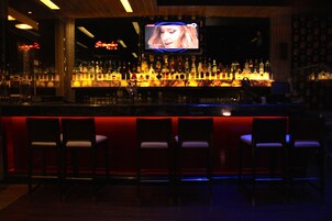 A bar area with a TV screen, multiple bottles, and bar stools.