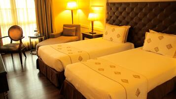 A hotel room with two beds, a chair, a small table, and lamps.