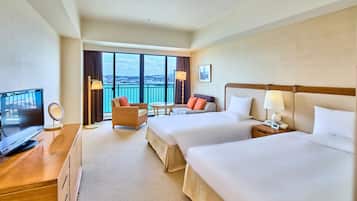 A hotel room with two beds, a TV, a desk, a chair, a balcony with a view, and a lamp.