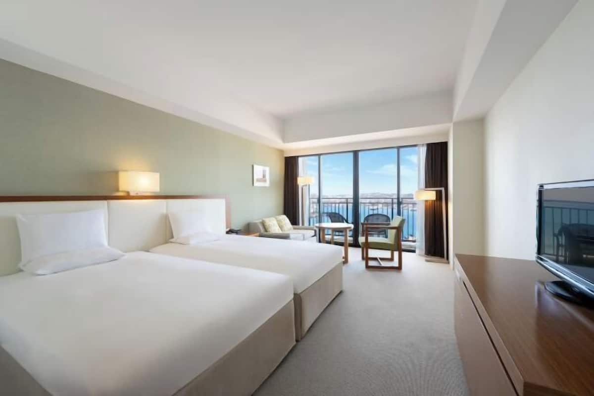 A hotel room with two beds, a TV, a balcony with a view, and a desk.