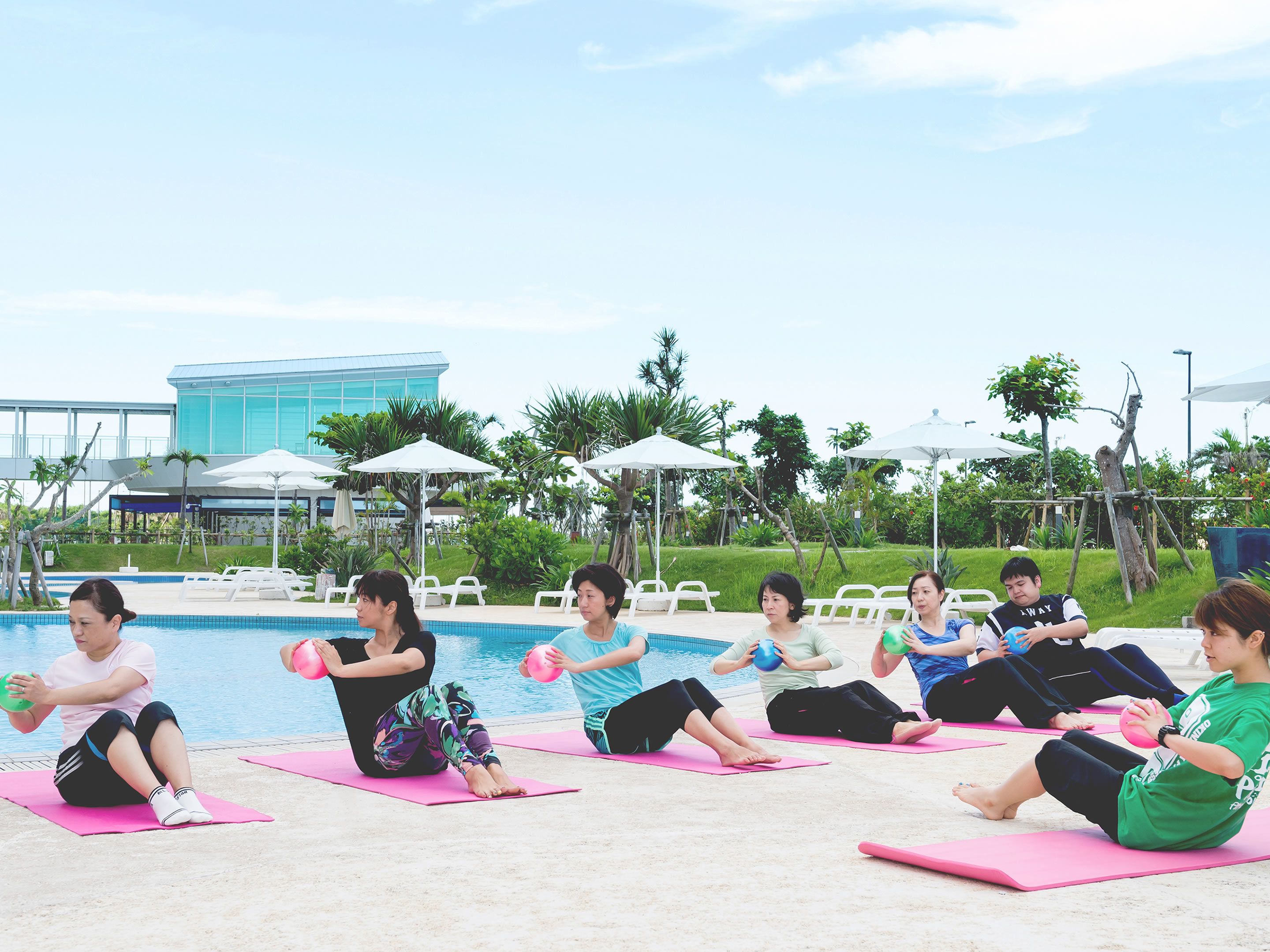 A group of people exercising by a pool with a modern building in the background.