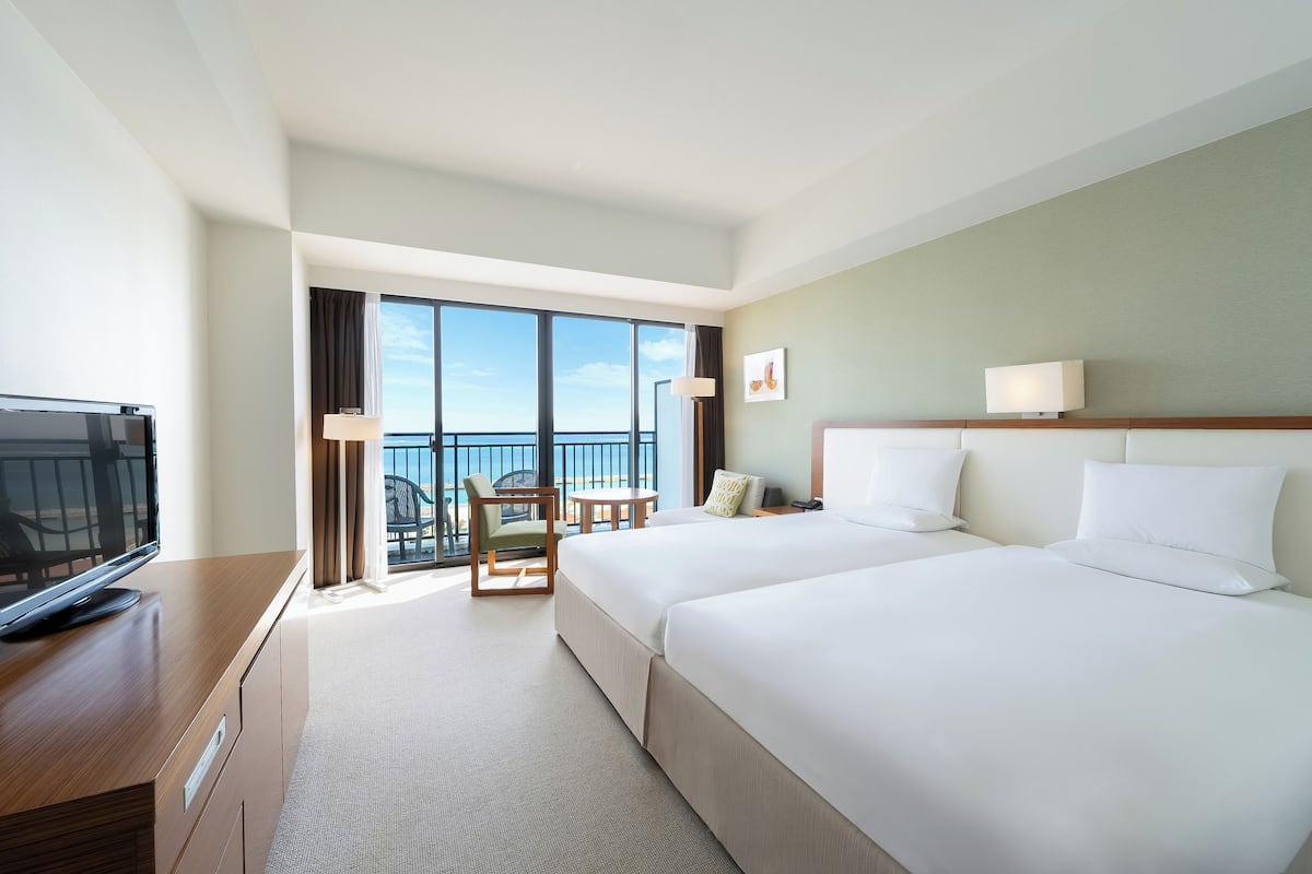 A hotel room with a large bed, a TV, a desk, and a balcony with a view.