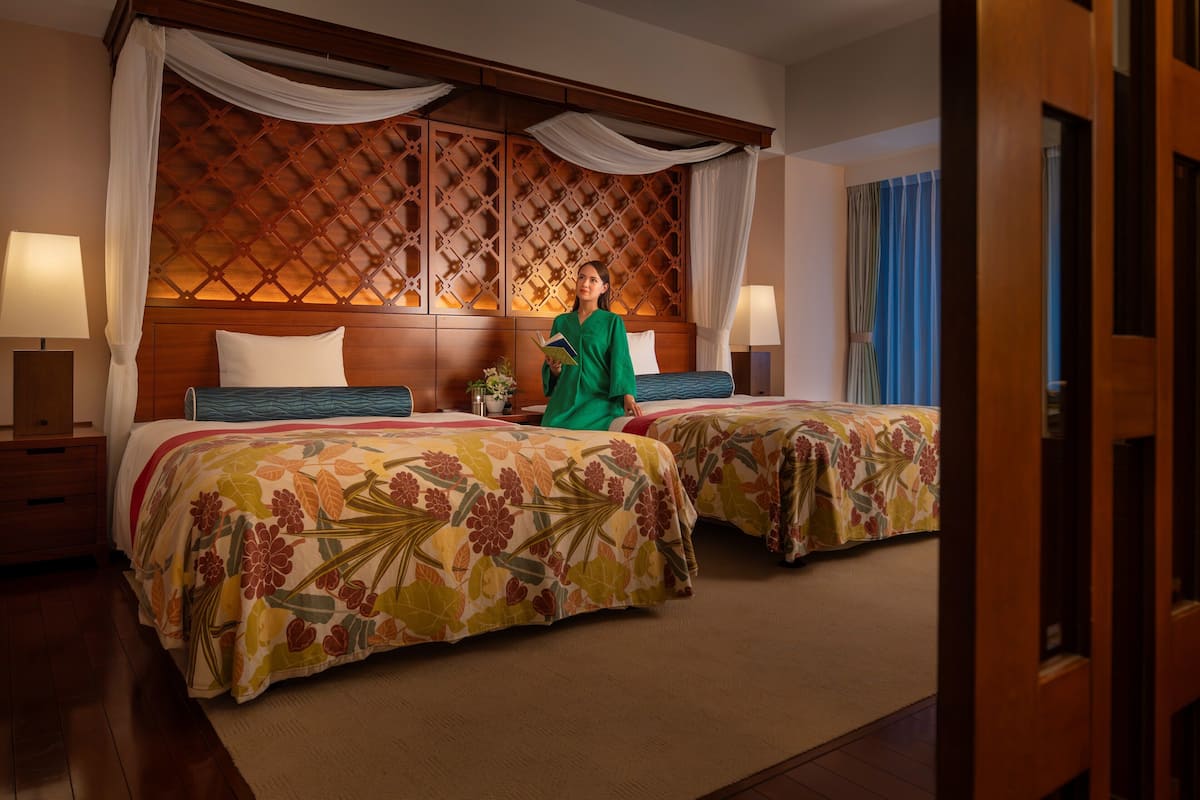 A hotel room with two beds, a wooden headboard, and a large window with curtains.