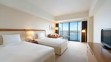 A hotel room with two beds, a TV, a balcony with a view, and a desk with a lamp.