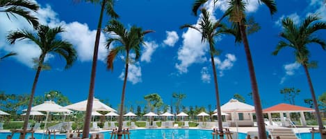 Een zwembadterras met palmbomen, ligbedden en parasols.