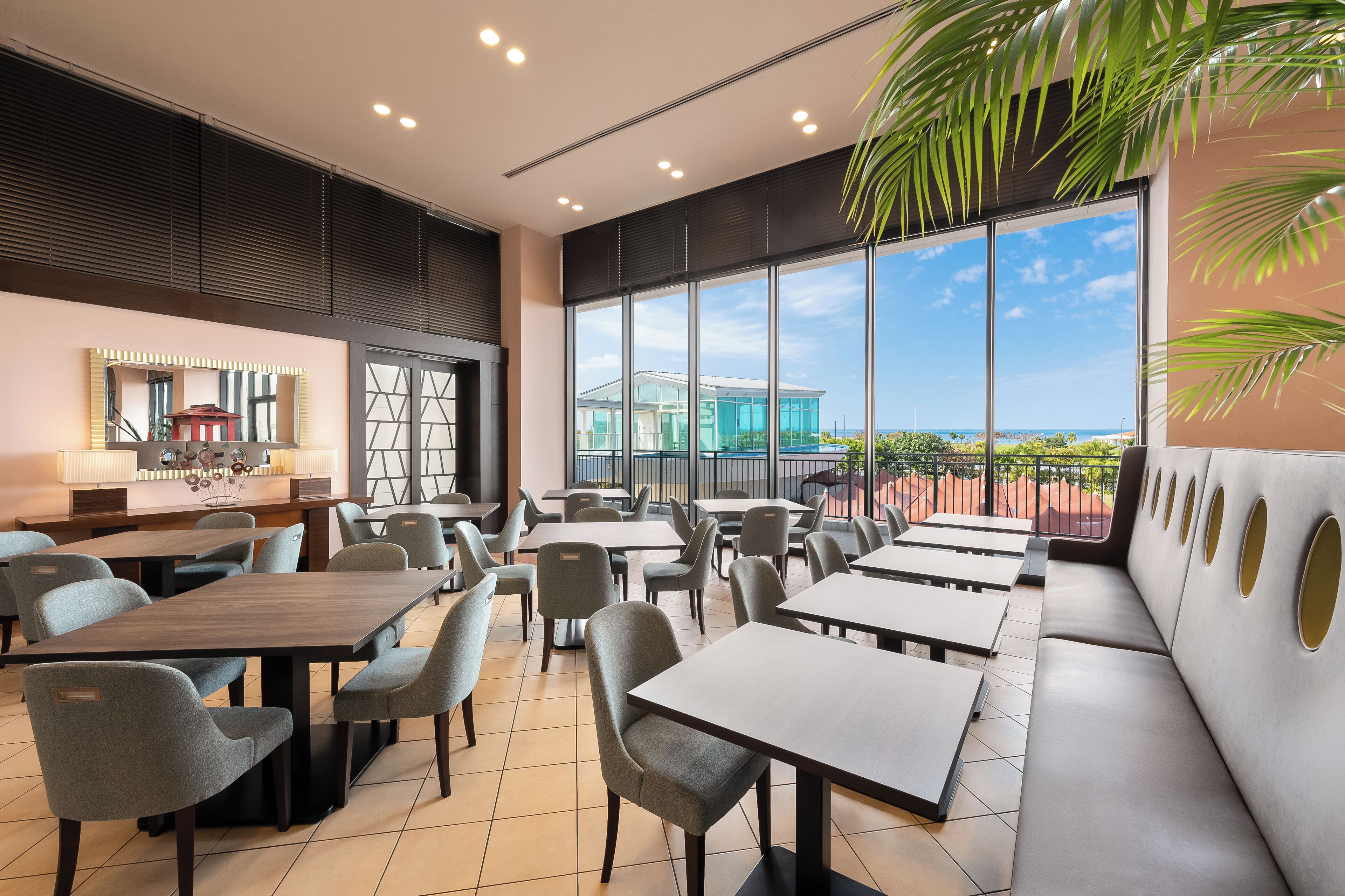 A modern dining area with tables and chairs, large windows, and a view of a building.