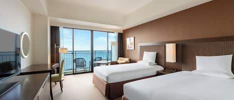 A hotel room with two beds, a desk, a chair, a small table, and a balcony with a view.