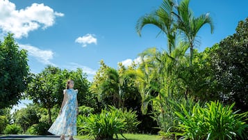 Una mujer con un vestido floral parada sobre un sendero pavimentado, rodeada de exuberante follaje y palmeras.