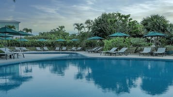 Una piscina con sillas de descanso y sombrillas, rodeada de vegetación.