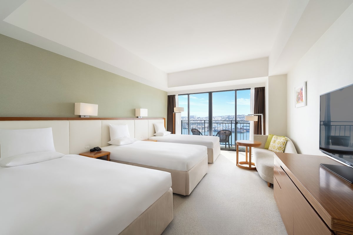 A hotel room with two beds, a TV, a desk, and a view of the city.