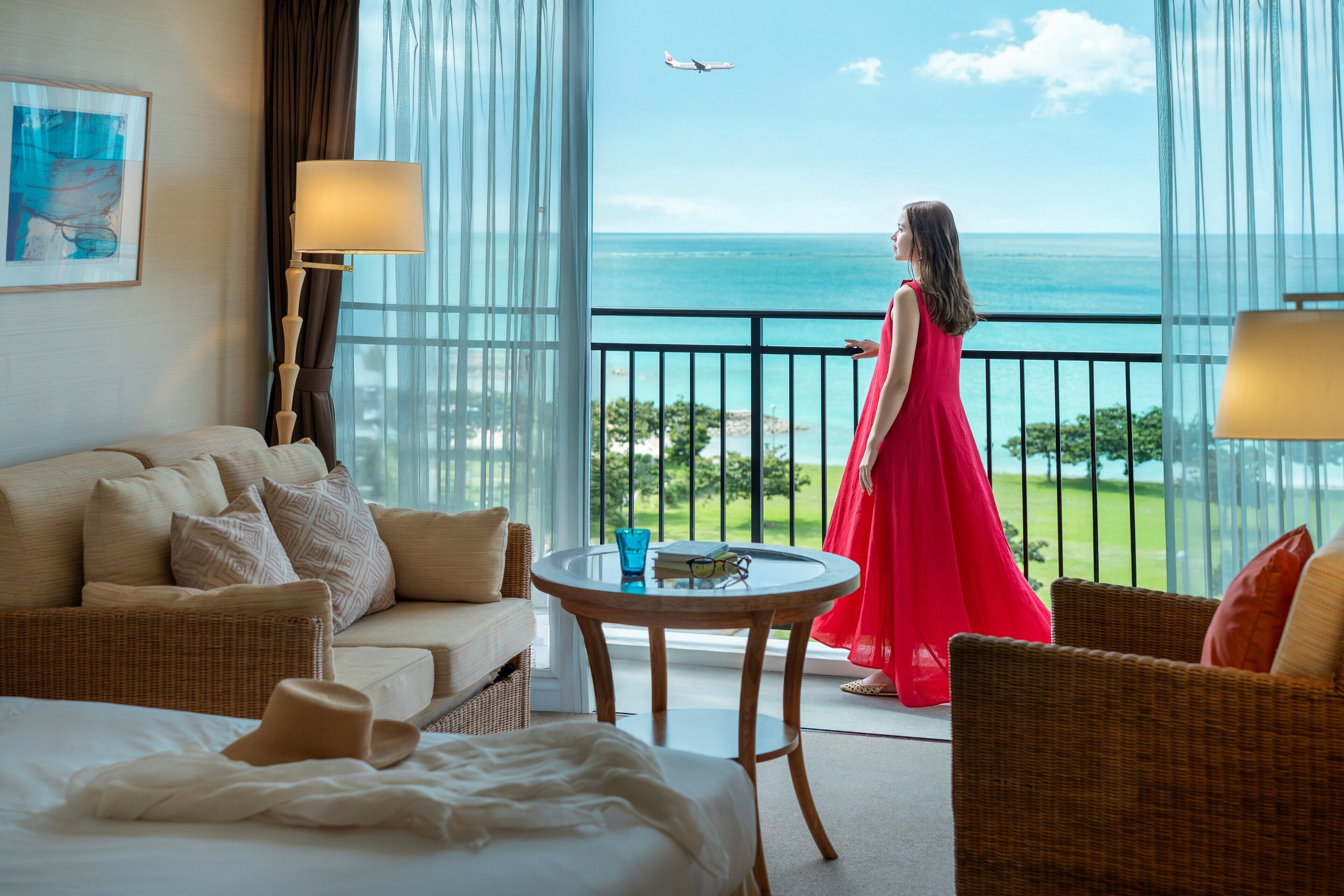 A hotel room with a balcony, a bed, a sofa, a table, and a view of the ocean.