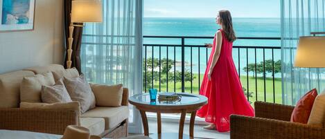 A hotel room with a balcony, a bed, a sofa, a table, and a view of the ocean.