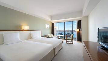 A hotel room with two beds, a desk, a chair, a TV, and a balcony with a view.