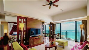 A spacious hotel room with a balcony, a TV, a dining table, and a sofa.