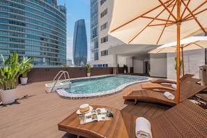 Ein Poolbereich auf dem Dach mit LiegestĂŒhlen, einem Whirlpool und einem groĂen Sonnenschirm.