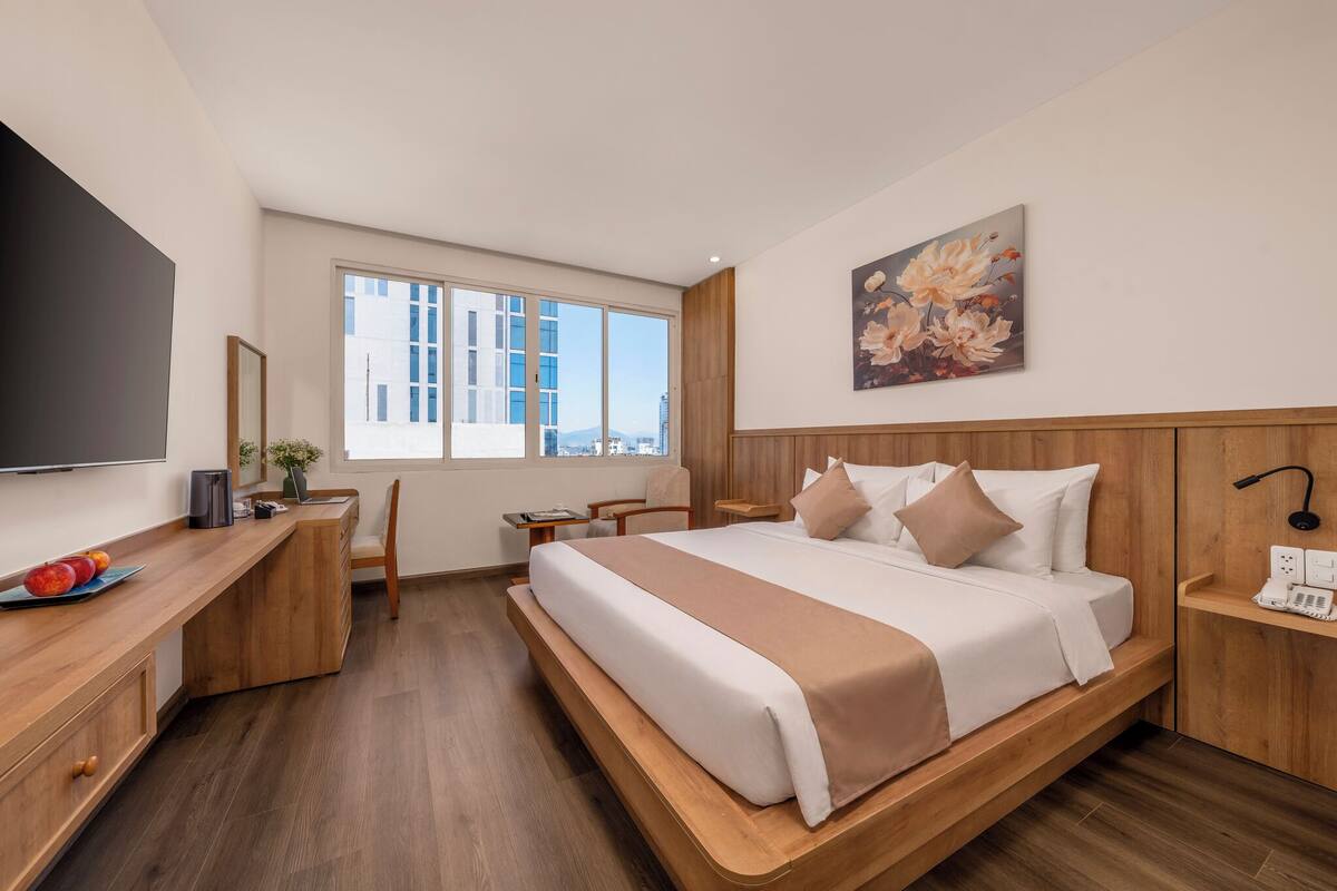 Quarto de hotel moderno com uma cama grande, secretária de madeira e vista para a cidade.