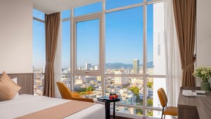 Una habitación de hotel con un ventanal grande, una cama, un escritorio y una silla.