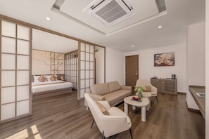 Ein modernes Hotelzimmer mit Bett, Sofa, Sessel, kleinem Tisch und einer Küchenzeile.