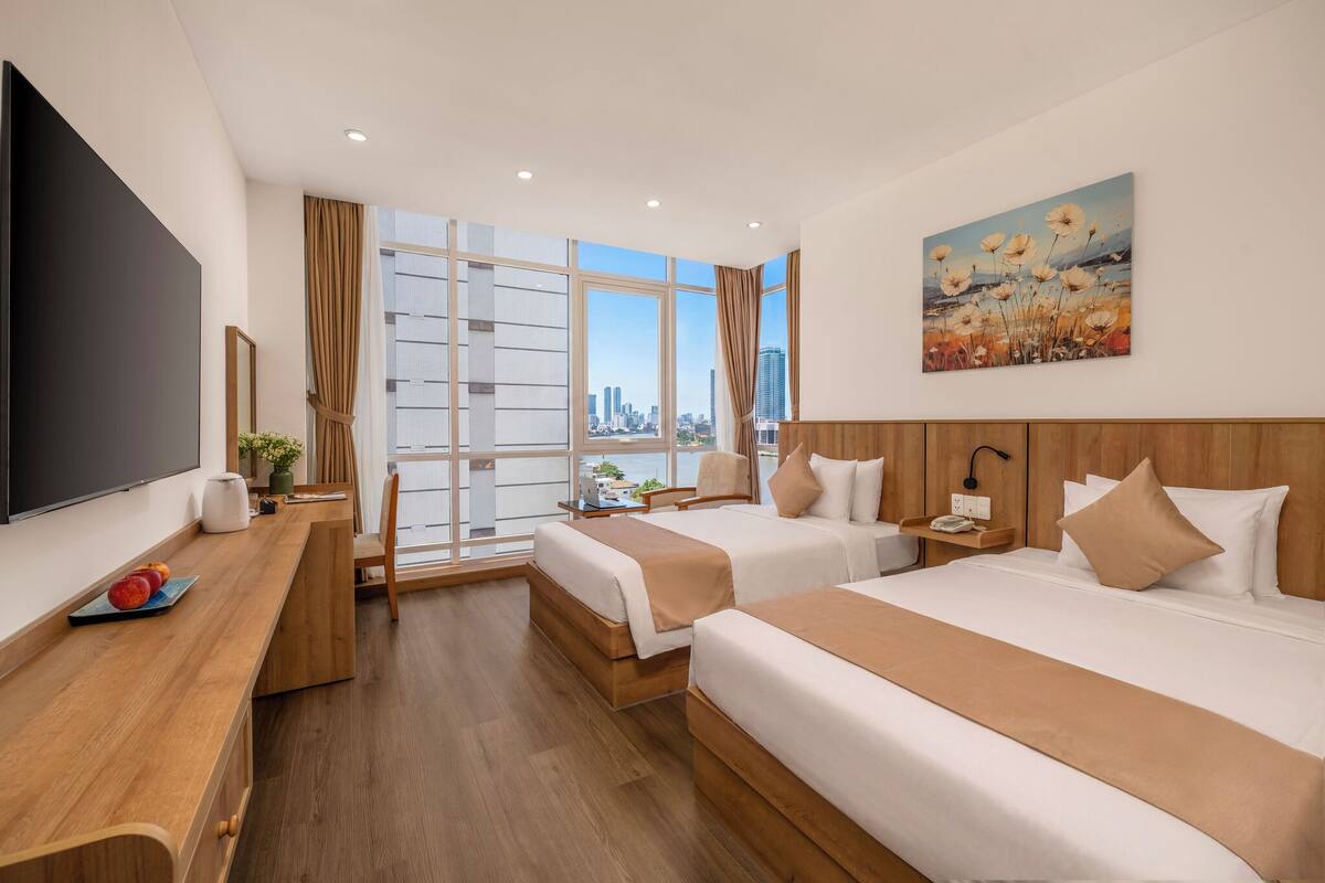 Quarto de hotel com duas camas, uma televisão, uma escrivaninha e um quadro.