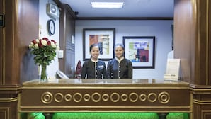 A reception area with a marble counter, framed artwork on the wall, and a clock. - Paladin Hotel (Baguio)