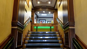 A grand staircase with ornate wood paneling and a green carpeted landing area. - Paladin Hotel (Baguio)