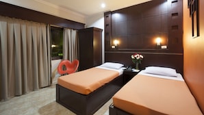 A hotel room with two single beds, a desk with a chair, a ceiling fan, and a window with curtains. - Paladin Hotel (Baguio)