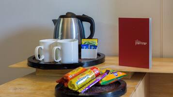 A coffee station with two white mugs, a kettle, and a red book titled 'MANA parivar' on a wooden table.