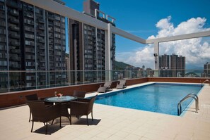 A rooftop pool with a glass balustrade, wicker chairs, and a table with a glass of wine. - Ramada Hong Kong Harbour View (Hong Kong)