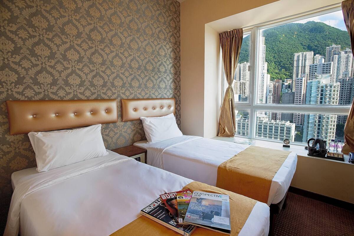 A hotel room with two beds, a window with a city view, and a magazine on the table.