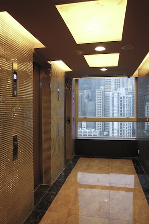 An elevator interior with reflective walls, a marble floor, and a large window offering a city view.