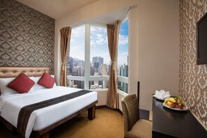 A hotel room with a large bed, a city view, a small desk with fruit, and patterned wallpaper. - Ramada Hong Kong Harbour View (Hong Kong)