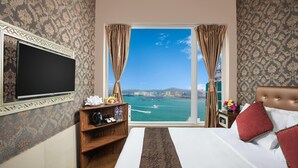 A hotel room with a bed, a TV, a desk with a coffee maker, a shelf with toiletries, and a view of the sea. - Ramada Hong Kong Harbour View (Hong Kong)