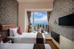 A hotel room with two beds, a TV, a window with curtains, and a view of a cityscape. - Ramada Hong Kong Harbour View (Hong Kong)