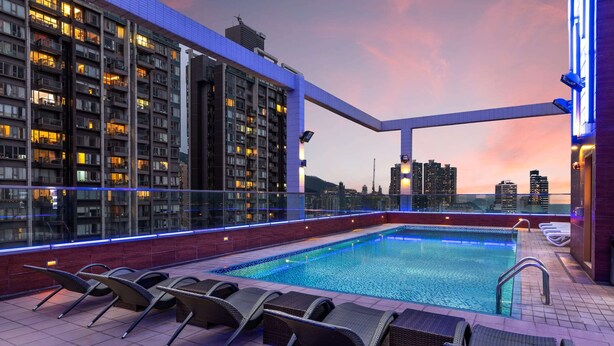 A rooftop pool area with lounge chairs, a swimming pool, and a city skyline view at dusk. - Ramada Hong Kong Harbour View (Hong Kong)