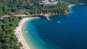 An aerial view of a coastal resort with a long sandy beach, a pier, and a large building with multiple balconies overlooking the sea.