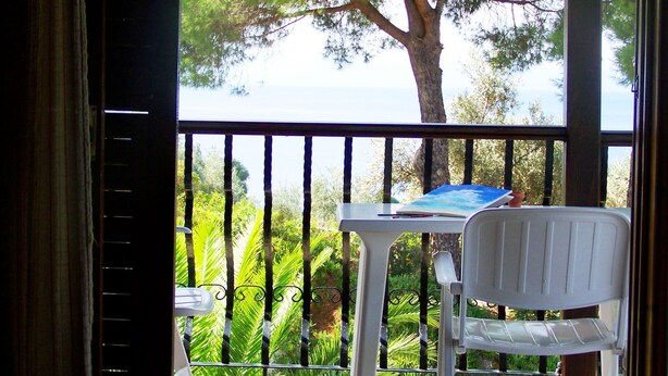 A balcony with a white chair and table, overlooking a lush green landscape and a body of water.