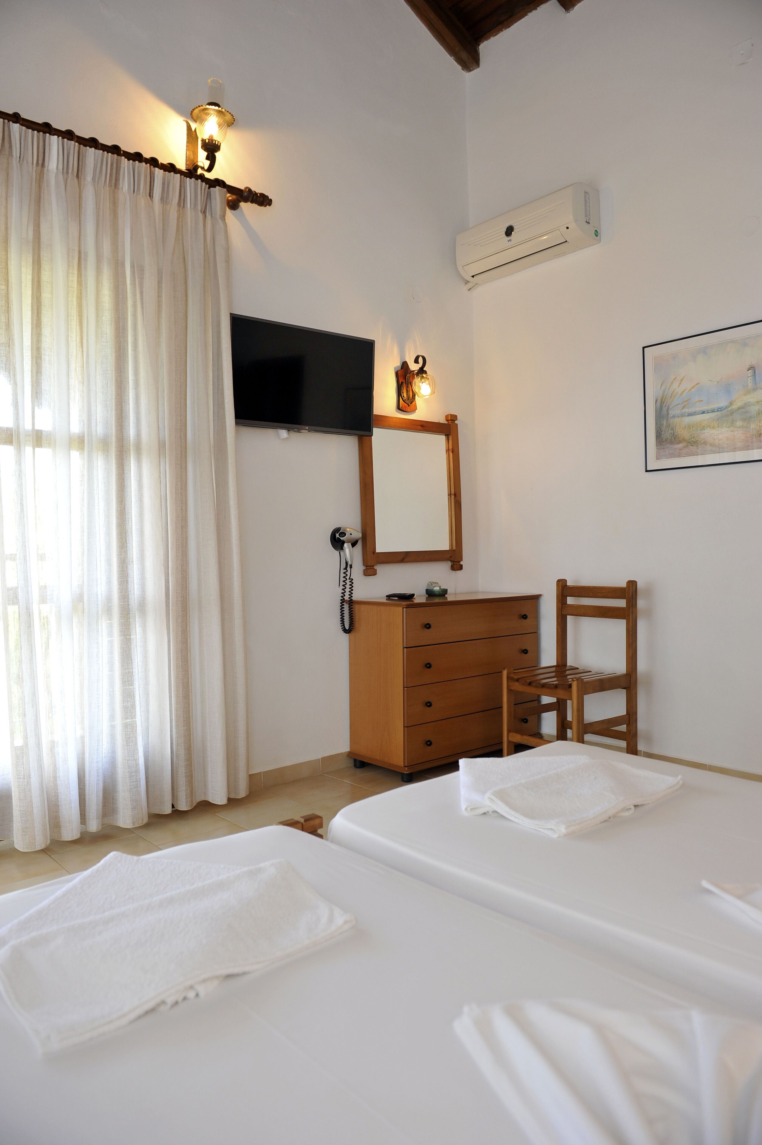A hotel room with two beds, a wooden dresser, a chair, a TV mounted on the wall, and an air conditioning unit.