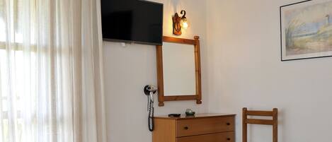 A hotel room with two beds, a wooden dresser, a chair, a TV mounted on the wall, and an air conditioning unit.