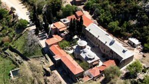 An aerial view of a historic building complex with multiple structures, including a large central building with a dome and smaller adjacent buildings with red-tiled roofs.