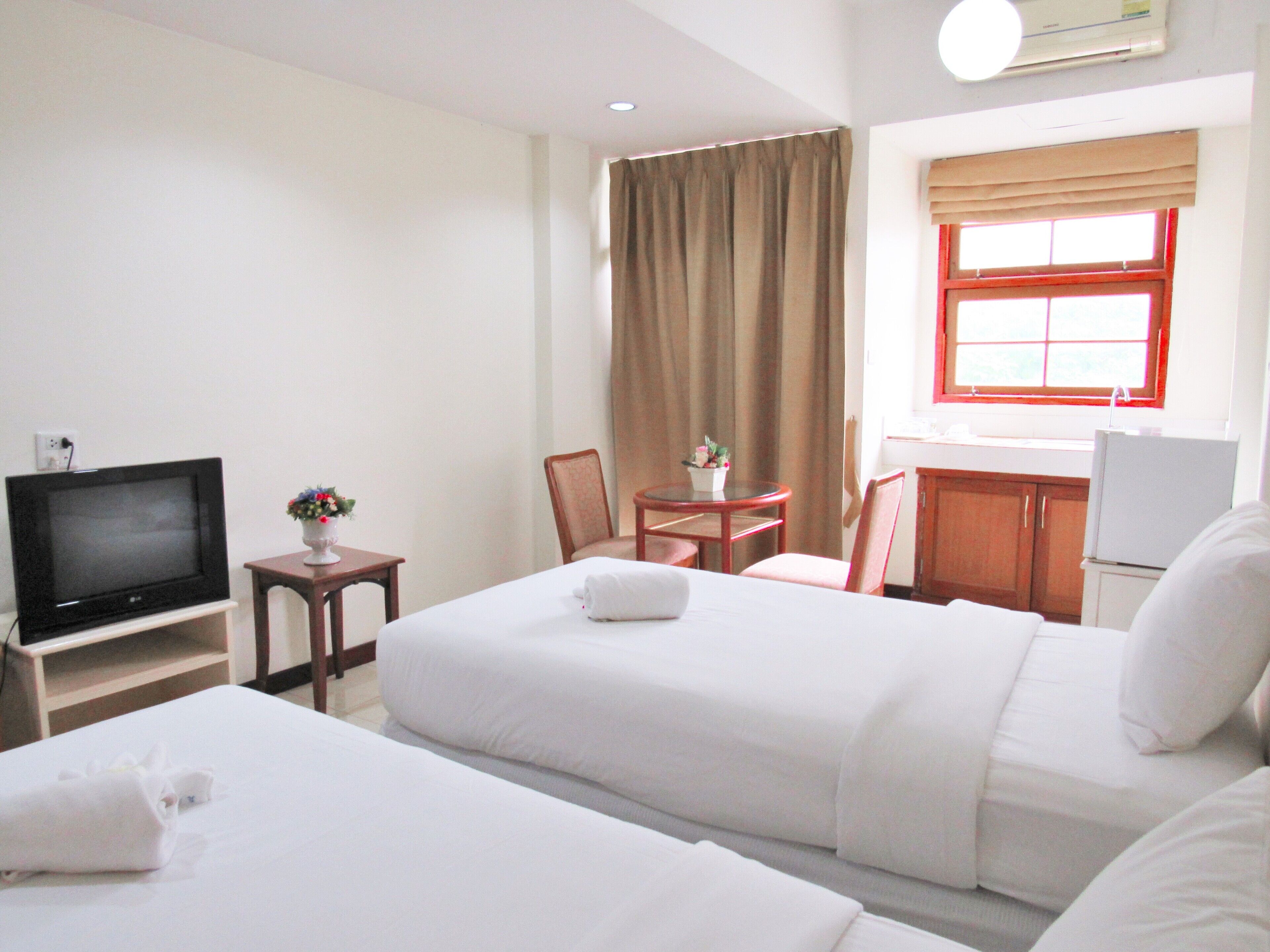 A hotel room with two beds, a TV, a small table with a plant, a chair, and a kitchenette.