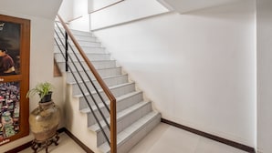 A staircase with white steps and a wooden handrail, leading to a landing with a large vase and framed pictures on the wall. - JL Bangkok (Bangkok)