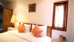 A hotel room with a bed, a nightstand, a lamp, a window with curtains, a painting on the wall, and a small table with flowers. - JL Bangkok (Bangkok)