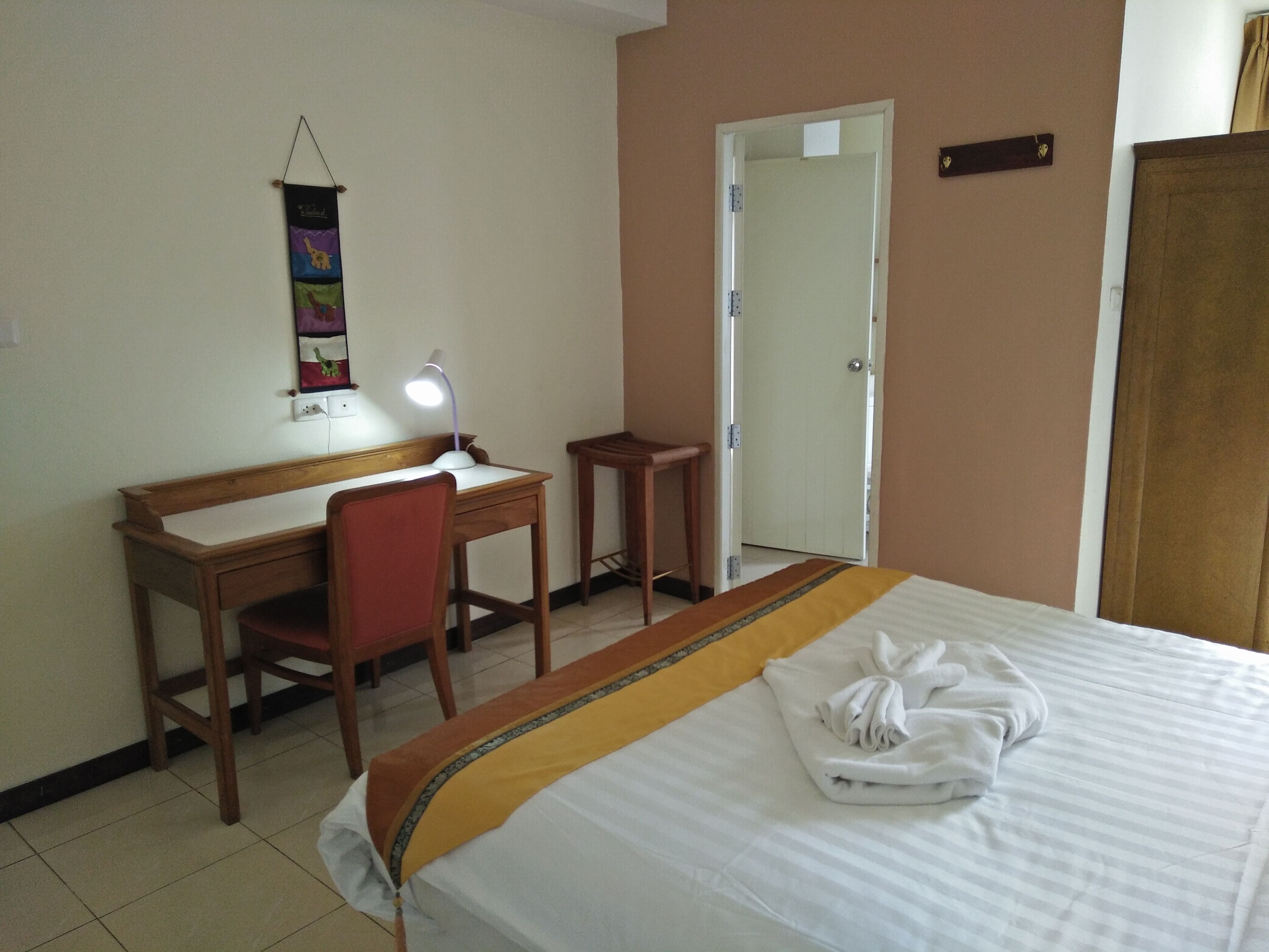 A hotel room with a bed, a desk, a chair, a lamp, and a door.