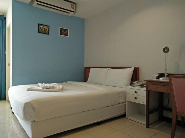 Una habitación de hotel con una cama individual, un escritorio con lámpara y dos pequeños cuadros en la pared.