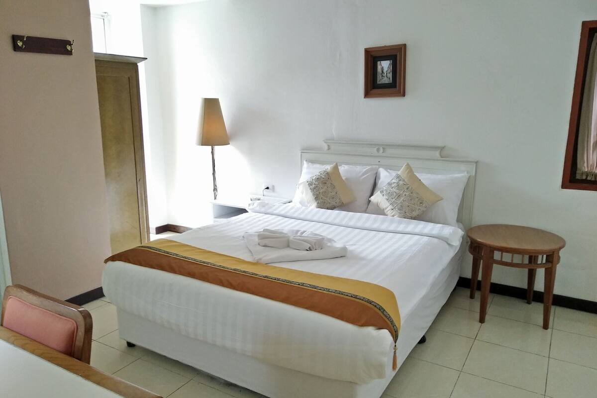 A hotel room with a large bed, a bedside table, a chair, and a small round table.