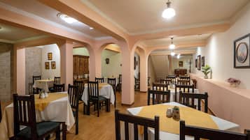 Un restaurante con varias mesas y sillas, pisos de madera y una paleta de colores cálidos.