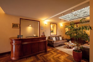 A hotel lobby with a reception desk, a sofa, a coffee table, and a large potted plant. - El Virrey by Katari  (Cusco)